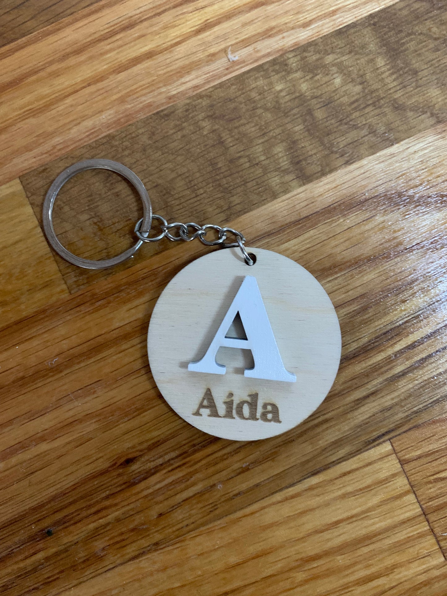 Llavero de madera personalizado con una inicial grande grabada y el nombre en la parte inferior.