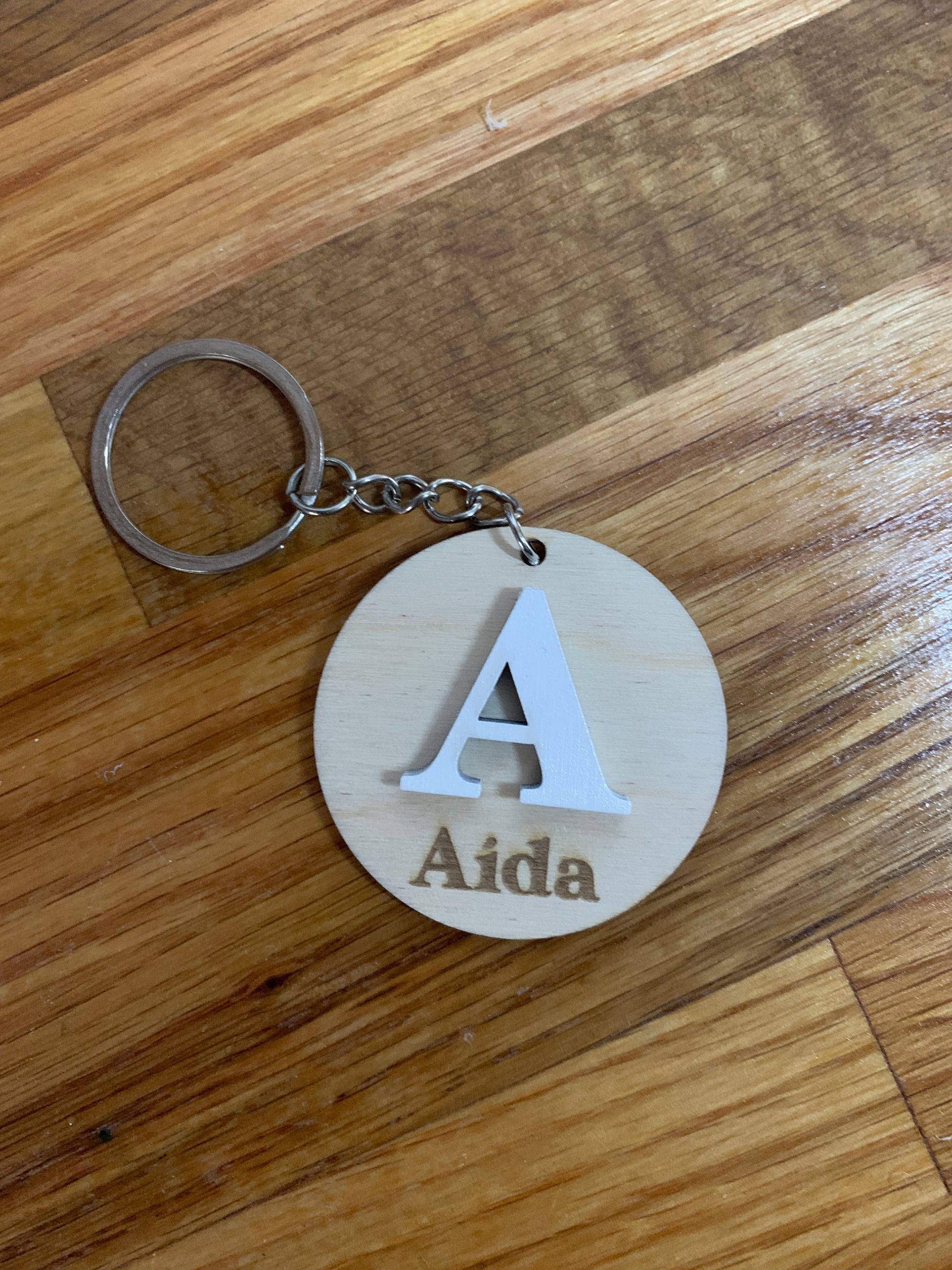 Llavero de madera personalizado con una inicial grande grabada y el nombre en la parte inferior.