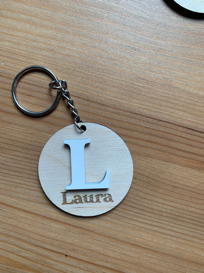 Llavero de madera con inicial sujetado en una mano, mostrando su tamaño y textura natural de la madera.