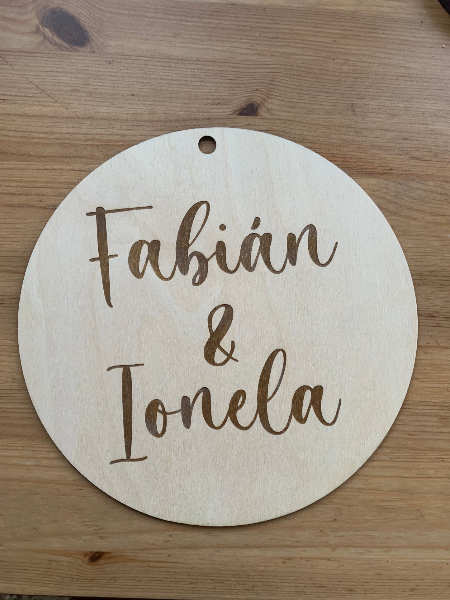 Círculo de madera personalizado con texto, exhibido en un entorno decorativo, destacando el orificio superior para colgar.