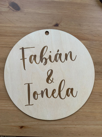 Círculo de madera personalizado con texto, exhibido en un entorno decorativo, destacando el orificio superior para colgar.