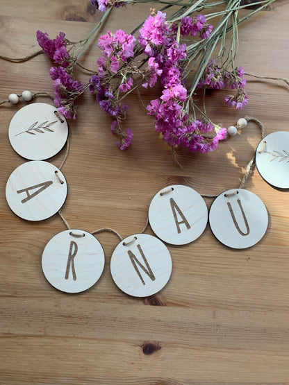 Guirnalda de madera personalizada con letras de nombre y figuras decorativas, como estrellas o nubes, colgada.