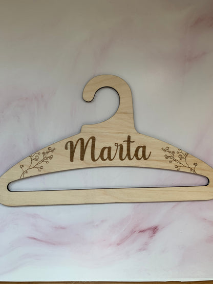 Percha de madera infantil con un conjunto de ropa de bebé colgado, mostrando su uso en un armario.